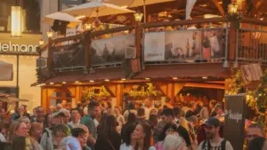 Viele Menschen stehen am Abend vor einer beleuchteten, zweistöckigen Holzkonstruktion auf einem Stadtfest.