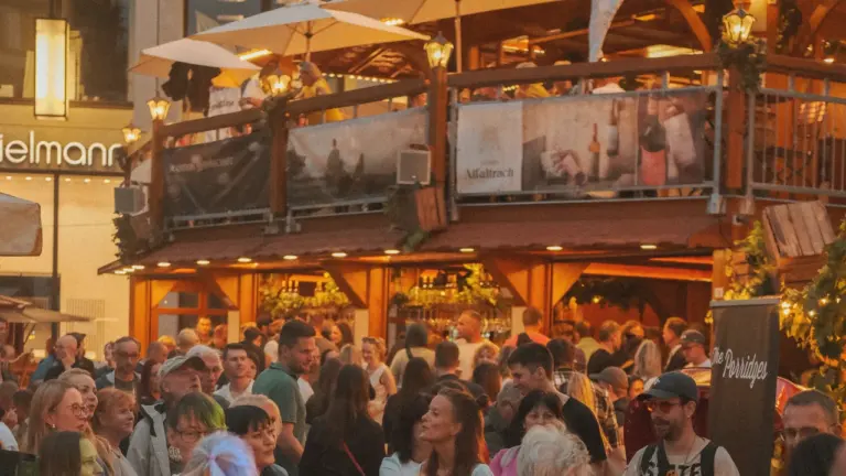 Viele Menschen stehen am Abend vor einer beleuchteten, zweistöckigen Holzkonstruktion auf einem Stadtfest.