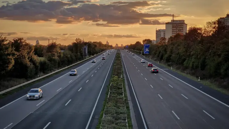 Autobahn bei Sonnenuntergang mit dichtem Verkehr und verschiedenen Fahrzeugen auf der Fahrbahn.