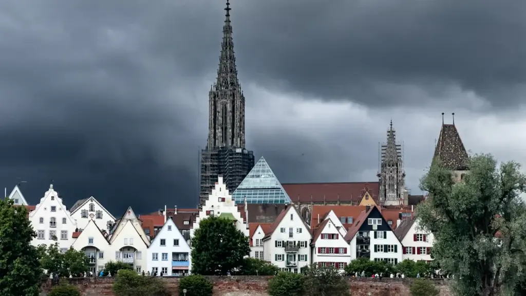 Dramatische Gewitterwolken über dem historischen Ulmer Münster und der Uferpromenade in Deutschland.