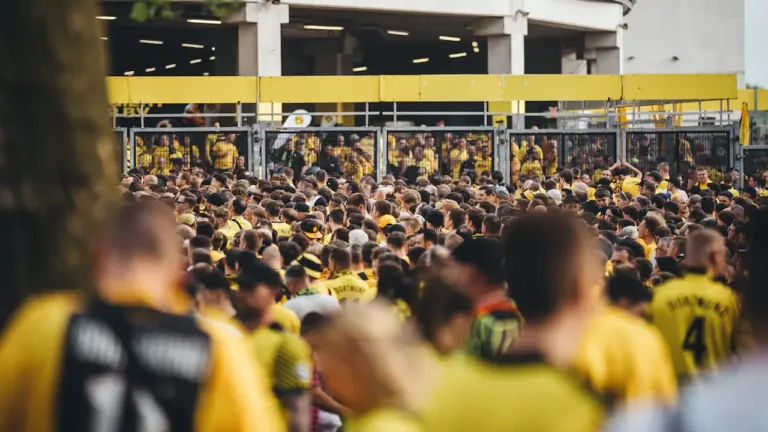 Fußballfans in gelben Trikots warten geduldig vor einem Stadion-Eingang in Deutschland.