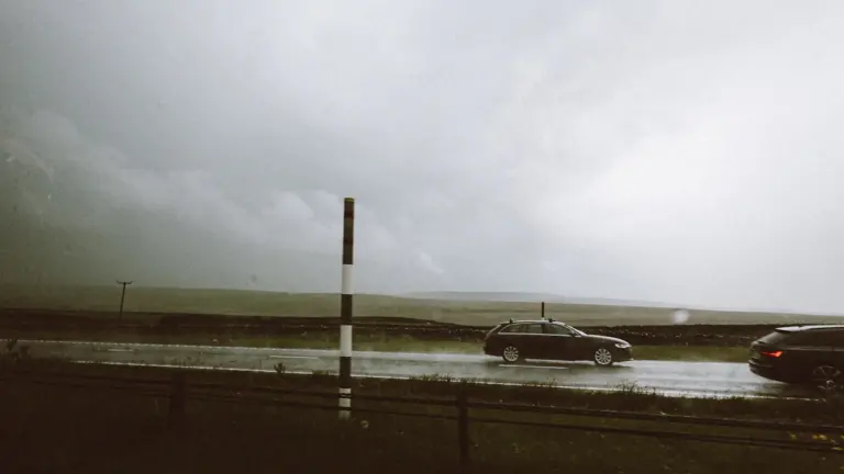 Autos fahren bei starkem Regen und schlechter Sicht über eine überflutete Landstraße.
