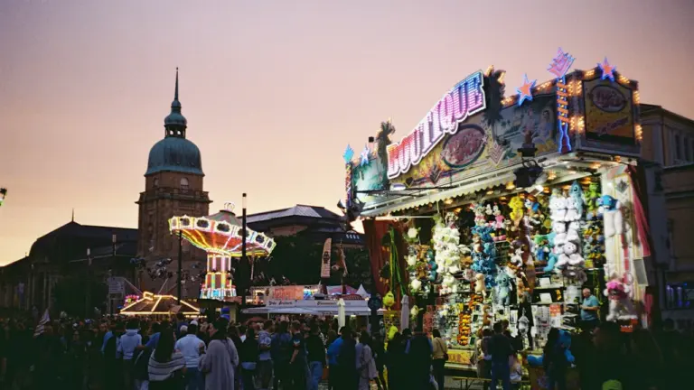 Jahrmarkt mit beleuchteten Ständen und Karussell bei Dämmerung in einer deutschen Stadt.
