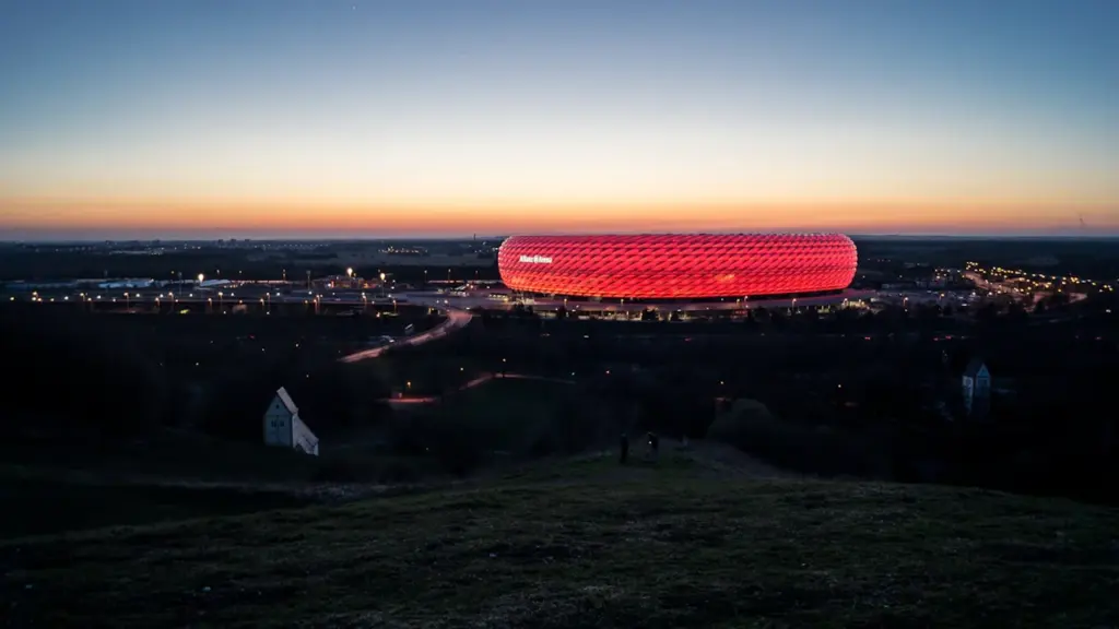 Die Allianz Arena bei Nacht in leuchtendem Rot vor einem dunklen Abendhimmel.