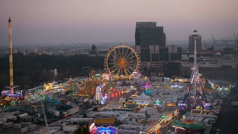 Weitwinkelaufnahme des Hamburger Doms bei Dämmerung mit beleuchtetem Riesenrad und Skyline.