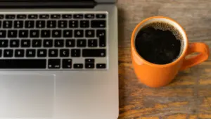 Laptop und eine Tasse Kaffee auf einem Holztisch im Büro während der Arbeitszeit.