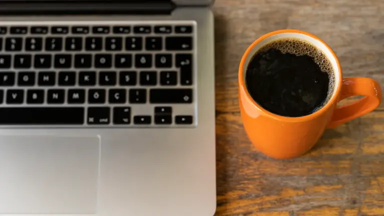 Laptop und eine Tasse Kaffee auf einem Holztisch im Büro während der Arbeitszeit.