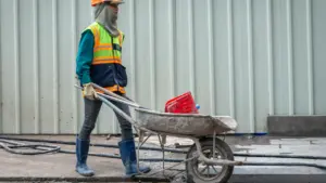 Bauarbeiter mit Schutzkleidung schiebt bei extremer Hitze eine Schubkarre auf einer Baustelle.