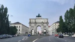 Münchens Siegestor an der Leopoldstraße bei Tageslicht mit umliegenden historischen Gebäuden und Straßenverkehr.