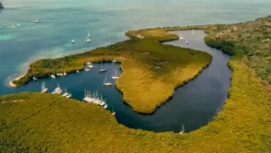 Luftaufnahme einer Bucht in der Karibik mit Segelbooten und üppiger Vegetation am Wasser.