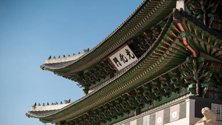 Detailaufnahme eines traditionellen koreanischen Palastdachs mit kunstvollen Verzierungen unter blauem Himmel.