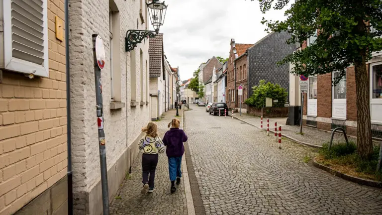 Zwei Kinder spazieren durch eine historische Kopfsteinpflasterstraße in einer nordrhein-westfälischen Stadt.