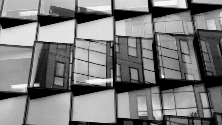 Abstrakte Schwarz-Weiß-Aufnahme einer modernen Glasfassade in München, die Reflexionen städtischer Architektur zeigt.