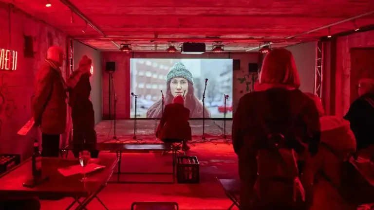 Menschen schauen in einem rot beleuchteten Raum einen Film auf einer großen Leinwand an.