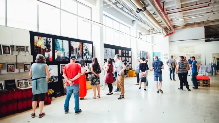 Besucher betrachten Kunstwerke in einer hellen, weitläufigen Galerie in einem industriellen Gebäude.