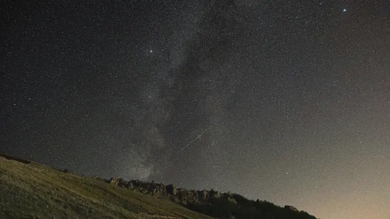 Sternenhimmel über einer grasbewachsenen Hügellandschaft bei klarer Nacht für astronomische Beobachtungen.