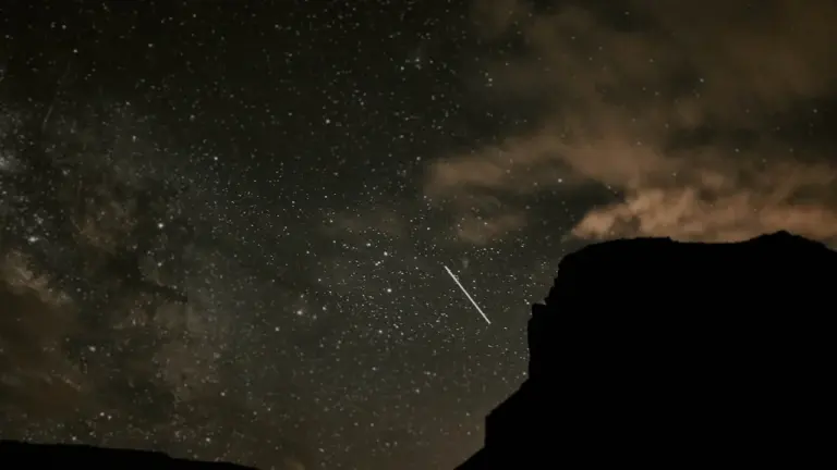 Dunkle Silhouetten eines Berges vor einem nächtlichen Sternenhimmel mit einer hellen Sternschnuppe.
