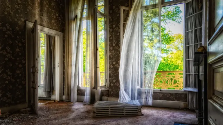 Ein offenes Fenster mit wehenden Vorhängen an einem heißen Sommertag in Deutschland.