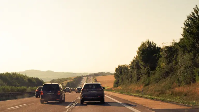 Autoverkehr auf einer deutschen Autobahn bei sonnigem Wetter und hügeliger Landschaft.