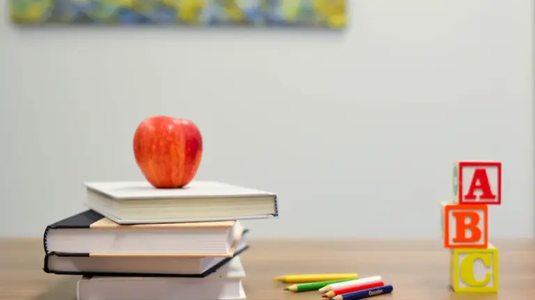 Ein roter Apfel auf einem Bücherstapel mit bunten Holzbuchstaben auf einem Schreibtisch.