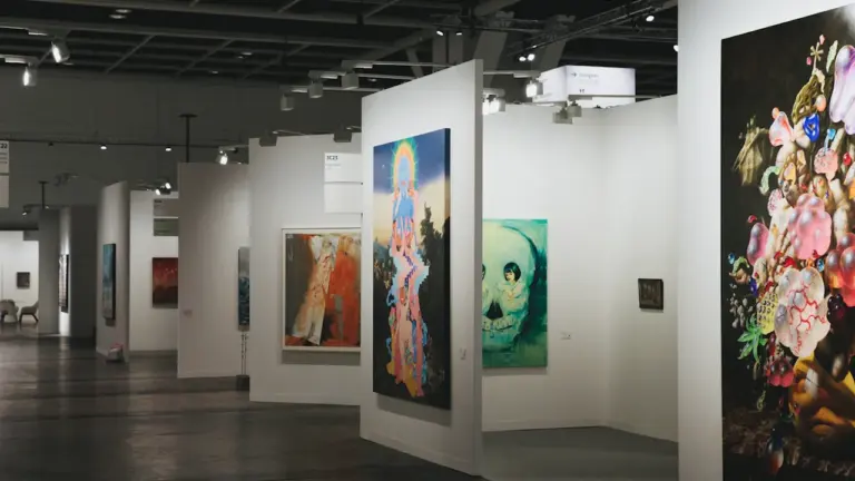 Blick in eine moderne Kunstgalerie mit zahlreichen Gemälden an weißen Stellwänden.