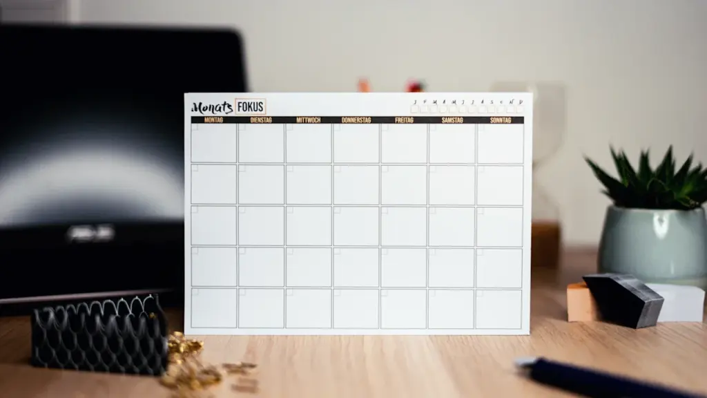 Ein leerer Schreibtischkalender auf einem Holztisch mit Büroartikeln im Hintergrund.