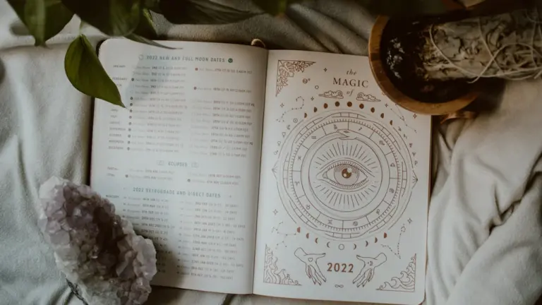Ein offenes Buch mit astrologischen Symbolen und Mondphasen auf einem weichen Stoff.