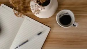Eine Tasse Kaffee neben einem leeren Notizbuch auf einem hölzernen Tisch.