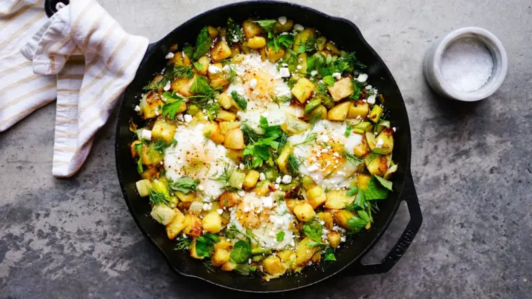 Eine gusseiserne Pfanne mit gebratenem Gemüse, frischen Kräutern und zerbröseltem Feta-Käse.