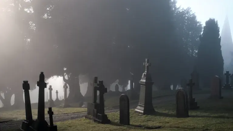 Nebelverhangener Friedhof mit alten Grabsteinen in einer melancholischen, stimmungsvollen Atmosphäre am Morgen.