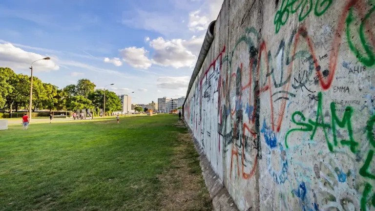 Die Berliner Mauer mit Graffitis vor einem modernen Berliner Hintergrundgebäude.