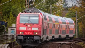 Roter Regionalzug auf den Gleisen vor einer herbstlichen Waldlandschaft in Deutschland.