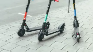 Drei auf einem Gehweg abgestellte E-Scooter vor einer städtischen Straße.