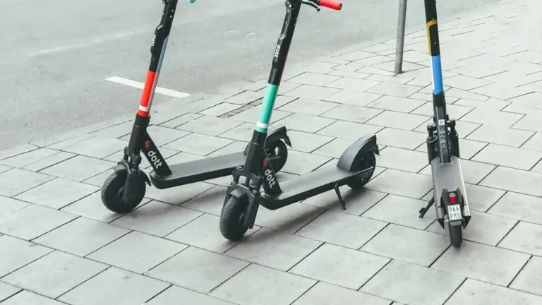 Drei auf einem Gehweg abgestellte E-Scooter vor einer städtischen Straße.
