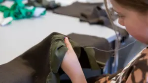 Ein junges Mädchen näht konzentriert Stoffstücke mit Nadel und Faden von Hand zusammen.