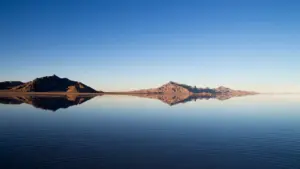 Spiegelbild eines Gebirges in ruhigem Wasser unter einem klaren blauen Himmel.