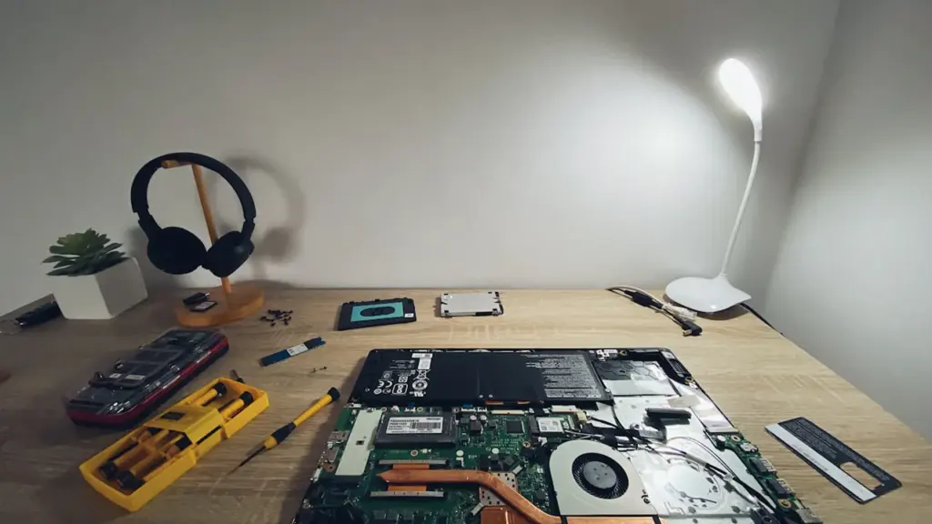 Ein offener Laptop auf einem Arbeitstisch zur Reparatur mit Werkzeug und Lampe.