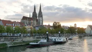 Der Regensburger Dom mit dem Museumsschiff am Ufer der Donau im Sonnenuntergang.