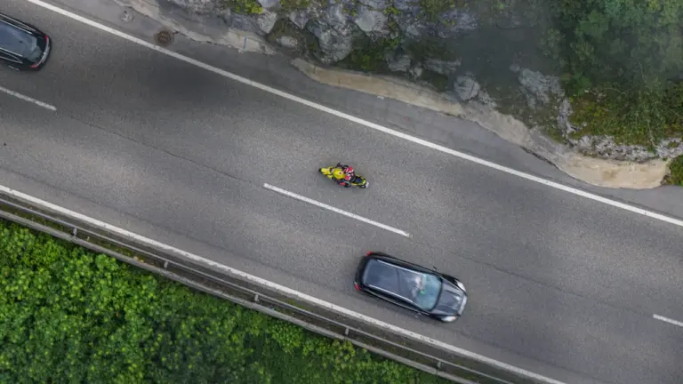 Ein Auto fährt auf einer kurvigen Straße neben einem grünen bewaldeten Hügel in Deutschland.