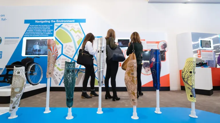 Menschen betrachten eine Ausstellung zur barrierefreien Mobilität in einem hellen öffentlichen Raum.