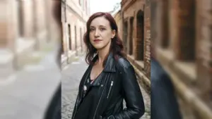 Eine junge Frau mit rötlichem Haar trägt eine schwarze Lederjacke in einer alten Gasse.