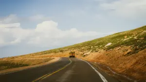 Ein gelber Schulbus fährt auf einer kurvigen Landstraße durch eine hügelige Landschaft.