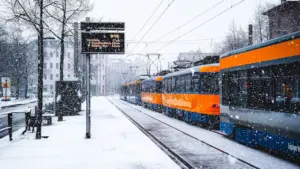 Eine orangefarbene Straßenbahn hält bei starkem Schneefall an einer Haltestelle in Leipzig.