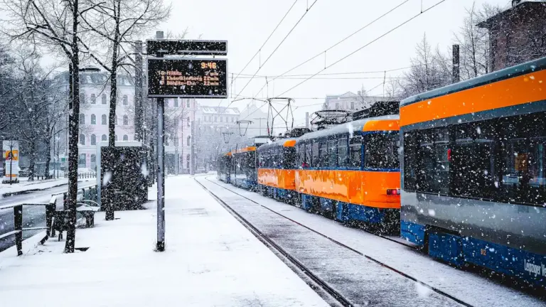 Eine orangefarbene Straßenbahn hält bei starkem Schneefall an einer Haltestelle in Leipzig.