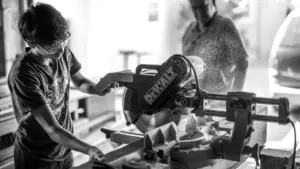 Ein junger Handwerker arbeitet konzentriert mit einer Kappsäge in einer Werkstatt.