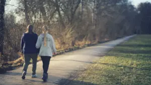 Zwei Personen gehen gemeinsam auf einem ruhigen Weg durch den Park spazieren.