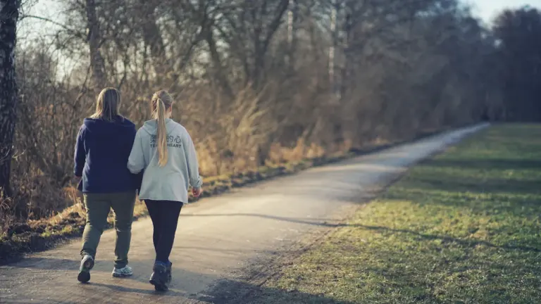 Zwei Personen gehen gemeinsam auf einem ruhigen Weg durch den Park spazieren.