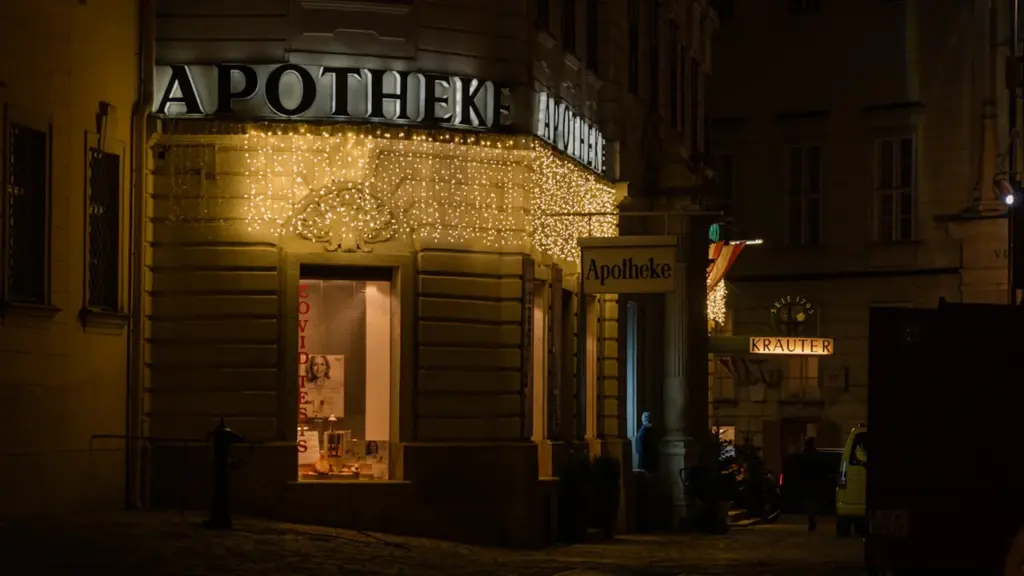 Eine abends beleuchtete Apotheke mit gut erkennbarem Schriftzug in einer städtischen Umgebung.