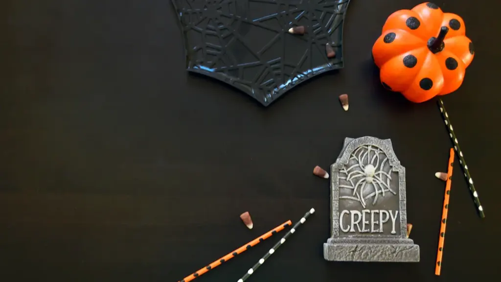 Dekorative Halloween-Requisiten mit Kürbis, Grabstein und Süßigkeiten auf schwarzem Hintergrund.