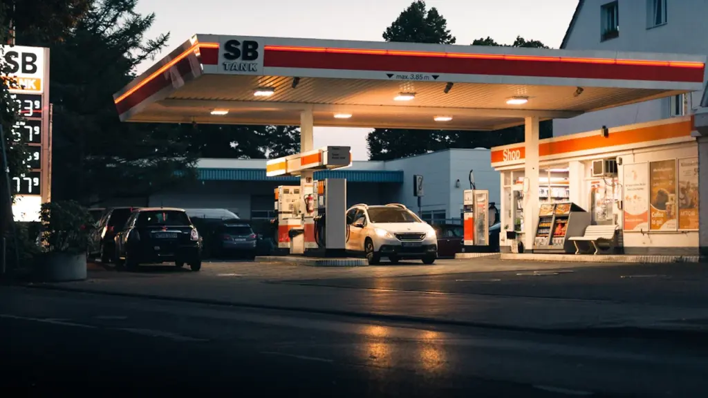 Eine typische deutsche Tankstelle bei Dämmerung mit Zapfsäulen und parkenden Autos.